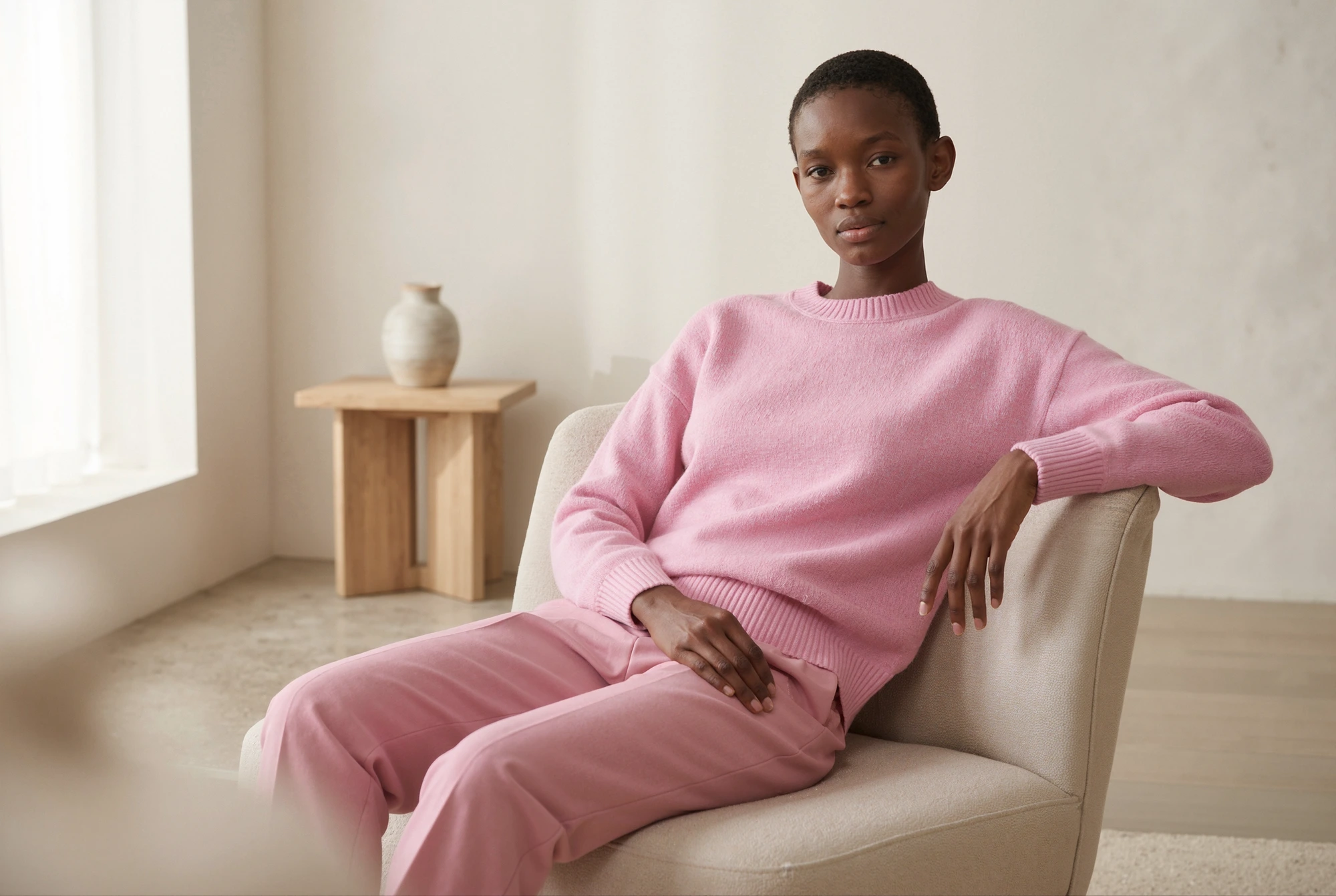 Model wearing a pink knit sweater, sitting in an armchair